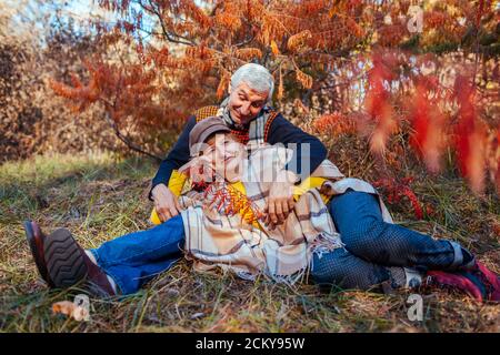 Activités familiales d'automne. Homme et femme âgés se détendant dans un parc d'automne, allongé sous un arbre. Les gens apprécient la nature Banque D'Images