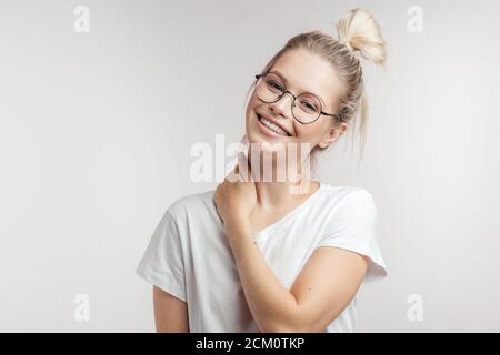 Jolie femme gaie de race blanche aux cheveux blonds attachés en chignon, looking at camera with friendly charmant sourire plus blanc studio isolé backgroun Banque D'Images