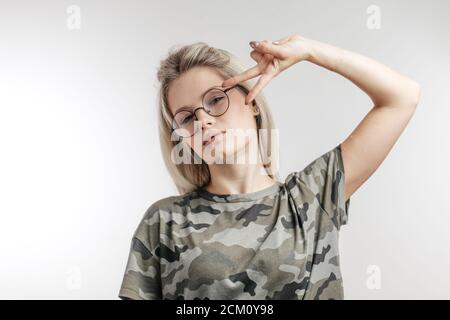 Belle jeune fille adolescente ou jeune femme dans la peinture éblouissante t-shirt faire signe de vicorée tout en regardant l'appareil photo, isolé sur fond blanc Banque D'Images