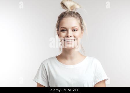 Jolie femme gaie de race blanche aux cheveux blonds attachés en chignon, looking at camera with friendly charmant sourire plus blanc studio isolé backgroun Banque D'Images