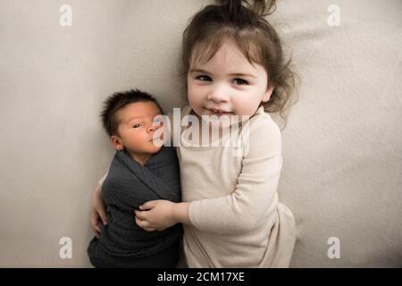 La grande sœur embrasse le nouveau-né bébé frère tout en étant allongé sur la couverture blanche Banque D'Images