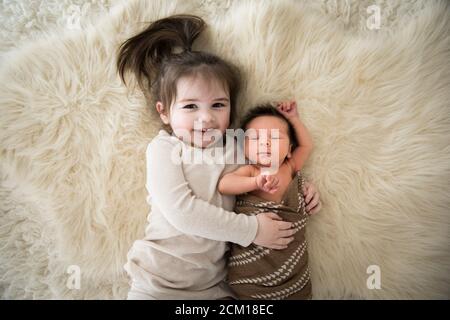 Happy Toddler Girl Snuggles nouveau-né frère, couché sur Fuzzy White Rug Banque D'Images