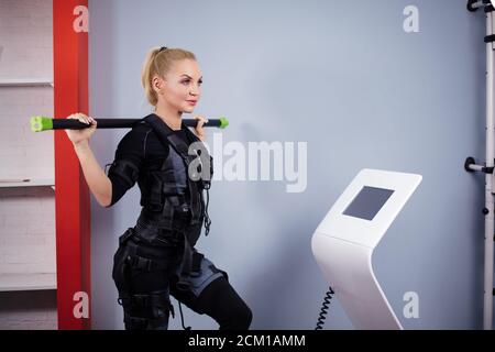 belle femme sportive tient le bâton pour stimuler les muscles du dos sur l'appareil ems. gros plan vue latérale photo.santé et bien-être concept Banque D'Images