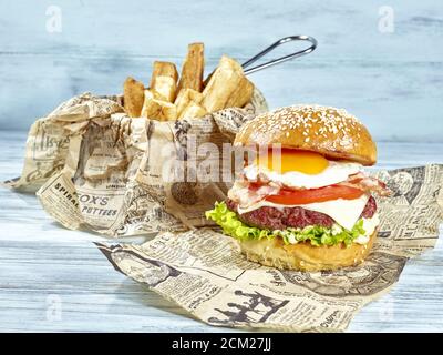 Hamburger aux œufs frit fait de pain au beurre avec de la laitue sur du mayonnaise, jus de hamburger et fromage, tomates fraîches nappées de bacon croustillant et f Banque D'Images