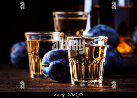 Slivovica - brandy de prune ou vodka de prune, liqueur dure, boisson forte dans des verres sur une table en bois ancienne, prunes fraîches, espace de copie Banque D'Images