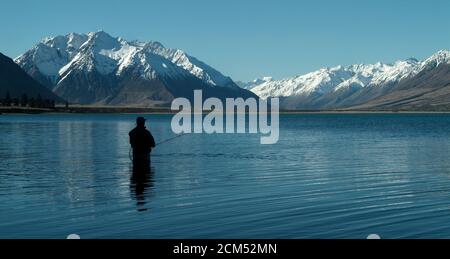 Pêche à la mouche, passage à gué dans le magnifique lac tranquille d'Ohau, Otago, South Island, Nouvelle-Zélande avec une vue sur la superbe neige couverte des Alpes du Sud Banque D'Images