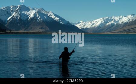 Pêche à la mouche, passage à gué dans le magnifique lac tranquille d'Ohau, Otago, South Island, Nouvelle-Zélande avec une vue sur la superbe neige couverte des Alpes du Sud Banque D'Images