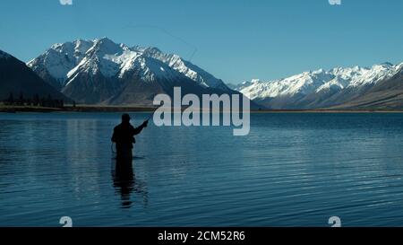 Pêche à la mouche, passage à gué dans le magnifique lac tranquille d'Ohau, Otago, South Island, Nouvelle-Zélande avec une vue sur la superbe neige couverte des Alpes du Sud Banque D'Images