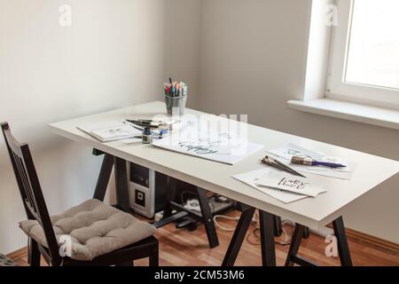 Feuilles de calligraphie, pointes, papier avec mots, encre et stylos sur table d'atelier Banque D'Images