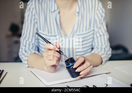 Gros plan de la main féminine trempant le stylo de calligraphie dans le puits d'encre Banque D'Images