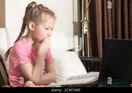 Enseignement en ligne à distance. Une écolière qui étudie à la maison avec un ordinateur portable et fait ses devoirs à l'école. Regarder attentivement l'écran d'un ordinateur portable. Corona Banque D'Images