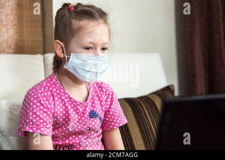 Enseignement en ligne à distance. Écolière portant un masque protecteur en quarantaine étudiant à la maison avec un ordinateur portable et faisant des devoirs à l'école. Coronavir Banque D'Images