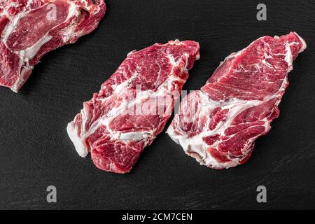 Viande de porc crue. Biftecks frais sur panneau d'ardoise sur fond noir. Vue de dessus, concept alimentaire Banque D'Images
