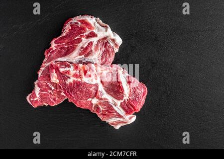 Steaks frais de viande de porc crue sur fond de pierre sombre, vue de dessus, un steak se trouve sur l'autre Banque D'Images