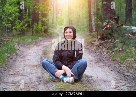 Homme dans la forêt. Une femme d'âge moyen est assise sur une route forestière. Banque D'Images