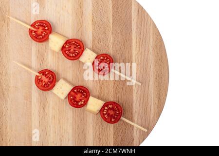 brochettes de fromage à la tomate sur une planche en bois, fromage avec trous découpés sur fond blanc Banque D'Images