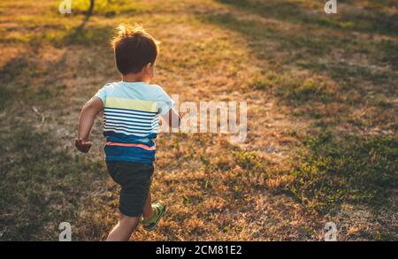 Petit garçon caucasien courant dans un champ pendant un été soirée à la campagne
