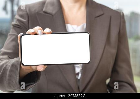 La main d'une femme montre un smartphone mobile avec écran blanc en position horizontale. Modèle mobile. Banque D'Images