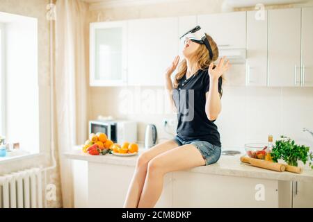 Une employée plutôt décontractée utilisant un casque de réalité virtuelle dans sa cuisine. Banque D'Images