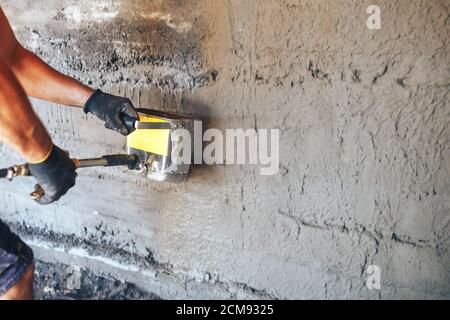 Homme plâtrage un mur avec du mortier à l'aide d'un seau de trémie Banque D'Images