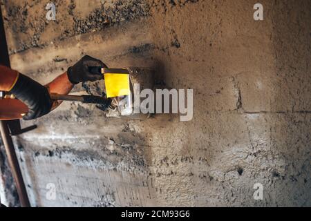 Homme plâtrage un mur avec du mortier à l'aide d'un seau de trémie Banque D'Images