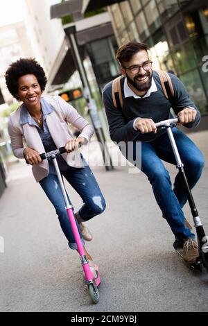 Deux hommes d'affaires souriants conduisant un scooter électrique au travail. Banque D'Images