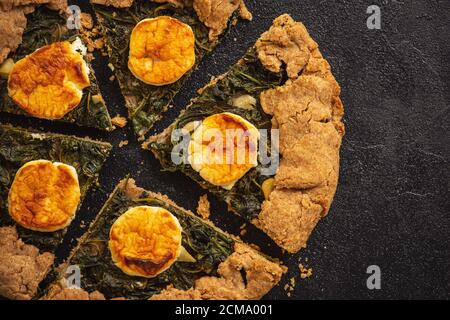 Galette rustique aux épinards et au fromage de chèvre sur fond noir. Banque D'Images