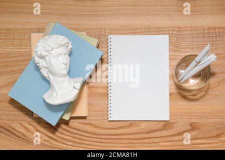 Carnet vide sur une table en bois avec des livres et une petite copie en plâtre de David faite en sculpture de buste de Chine. Vue de dessus avec espace de copie, plan de travail. Éducation et Banque D'Images