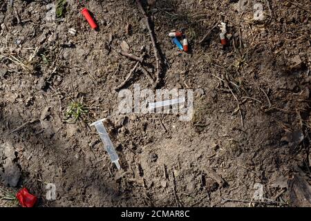 Une aiguille, une seringue, un capuchon et des comprimés médicaux cassés utilisés se trouvent sur le sol dans un parc de la ville Banque D'Images