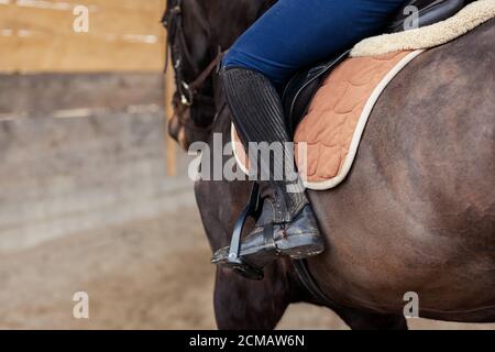 Gros plan d'une femme dans un équipement de conduite assis dans un selle sur un cheval marron sur le terrain d'entraînement Banque D'Images