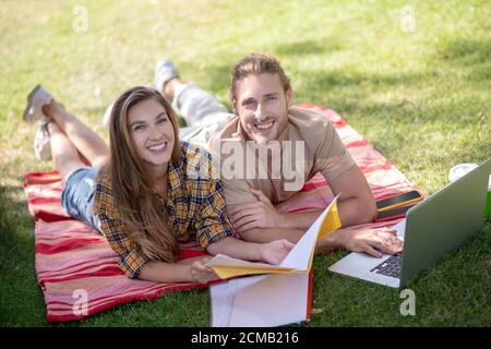 Jeune couple heureux allongé sur l'herbe et étudiant Banque D'Images