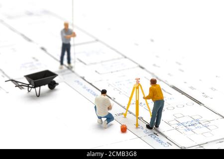 Le technicien d'arpenteur de personnes miniatures mesure la distance pour construire une maison sur un plan de dessin. Banque D'Images
