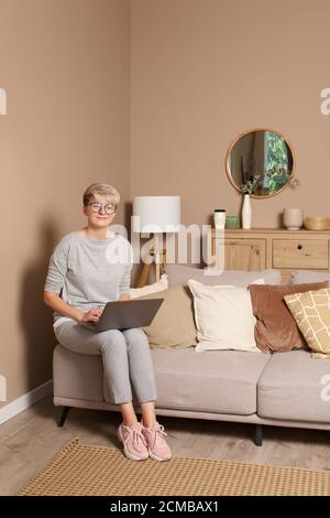 Jeune femme heureuse freelance travaillant ou apprenant à la maison. Portrait complet du corps de la femme jolie intelligente environ 30s dans des vêtements et des lunettes décontractés si Banque D'Images