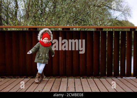 Jolie petite fille en vêtement d'extérieur chaud dansant et s'amuser dans la rue en automne ou en hiver, plein corps Banque D'Images