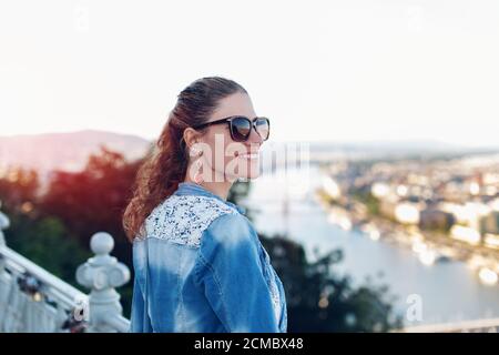 Jeune femme se demandant dans le panorama de la ville depuis la colline au coucher du soleil Banque D'Images