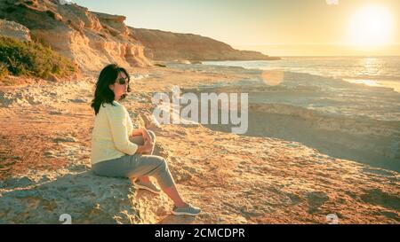 Femme assise sur la plage et profitant du coucher du soleil à Port Noarlunga, Australie méridionale Banque D'Images