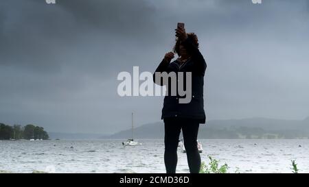 Femme prenant le selfie au lac Windermere le jour gris humide Banque D'Images