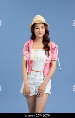 Portrait d'une jeune femme asiatique portant un chapeau, un t-shirt, un Jean court et une veste rose isolée sur fond bleu. Banque D'Images