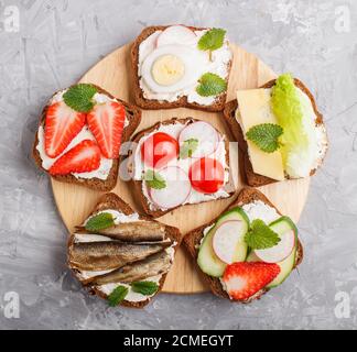 Ensemble de différents sandwiches avec fromage, radis, laitue, fraise, crarats, tomates et concombres sur bois sur fond de béton gris Banque D'Images