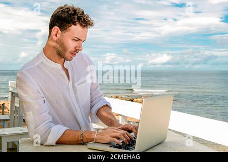 beau et réussi homme caucasien travaillant avec un ordinateur portable sur la plage. freelance et travail à distance. étudiant sur la rive méditerranéenne Banque D'Images