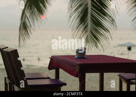 Restaurant en plein air romantique table et chaises à la plage au coucher de soleil avec des feuilles de plam Banque D'Images