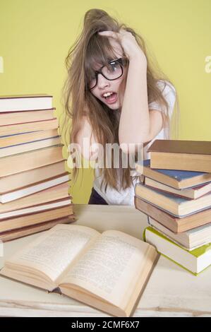 Fille assise avec beaucoup de livres et saisit sa tête. Banque D'Images