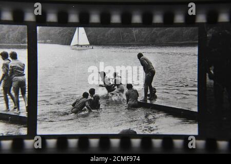 Belle photographie en noir et blanc vintage des scouts de mer des années 70 se poussant les uns les autres dans l'eau d'un quai tout en scouting dans le camp de scouts d'été. Banque D'Images