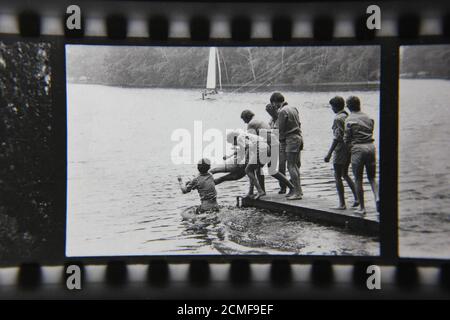 Belle photographie en noir et blanc vintage des scouts de mer des années 70 se poussant les uns les autres dans l'eau d'un quai tout en scouting dans le camp de scouts d'été. Banque D'Images