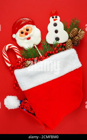 Chapeau de père Noël avec bonbons de Noël traditionnels sur fond rouge. Flat lay, vue de dessus Banque D'Images