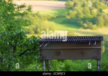 Vider le barbecue portatif devant un paysage d'été vert frais, en gros plan Banque D'Images