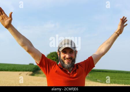 un homme à barbe heureux a soulevé ses mains au ciel dans un grain d'été doré, à bras ouverts. Banque D'Images