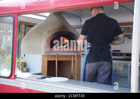 chef qui retire la pizza chaude du four à bois dans une camionnette à pizza mobile. Banque D'Images