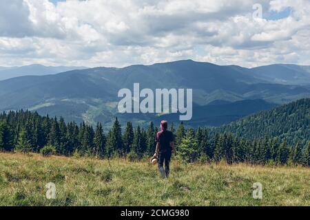 Fille aux cheveux roses debout sur la clairière et regarde les montagnes. Randonnée dans la forêt en été. Forêt d'automne sombre. Concept de voyage local Banque D'Images