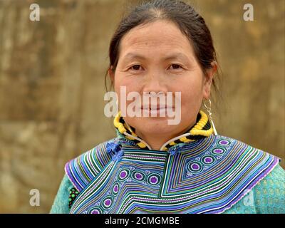 La femme de la tribu des collines de Hmong, une fleur vietnamienne d'âge moyen, porte une tenue de nuit traditionnelle brodée en bleu et pose pour la caméra. Banque D'Images